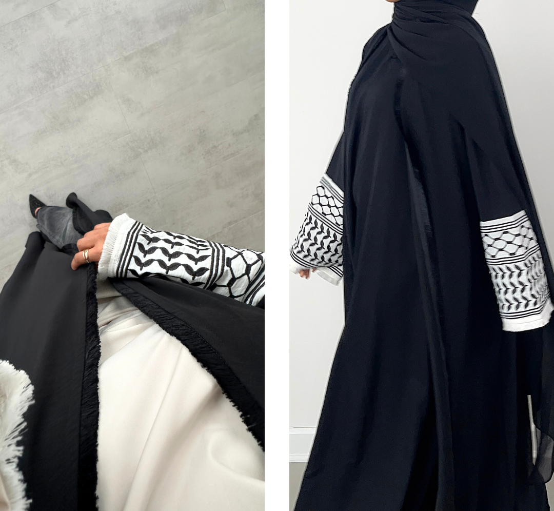 Black abaya with white keffiyeh patterned sleeves held by a person against a neutral background